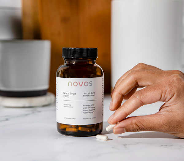 Persona tomando cápsula de NOVOS Boost NMN como suplemento diario para apoyar niveles de NAD+, energía celular y envejecimiento saludable